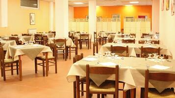 A dining area with multiple tables and chairs, each set with tablecloths and cutlery.