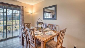 Un coin repas avec une table en bois dressée pour quatre personnes, entourée de chaises en bois. Une grande fenêtre offre une vue sur l’extérieur.