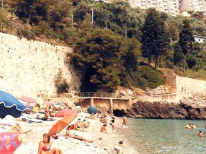 Una playa con gente tomando el sol y nadando, sombrillas y un acantilado rocoso al fondo.