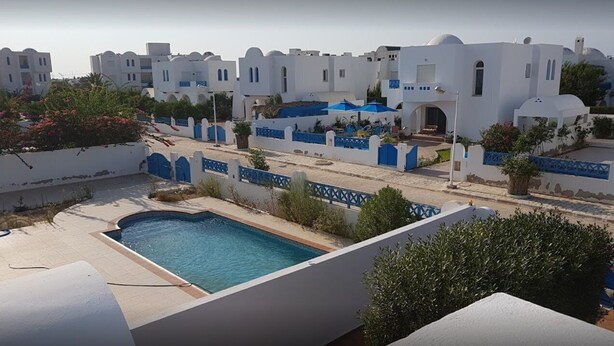 Zona de piscina con vista despejada a edificios blancos con detalles azules y una cerca azul.