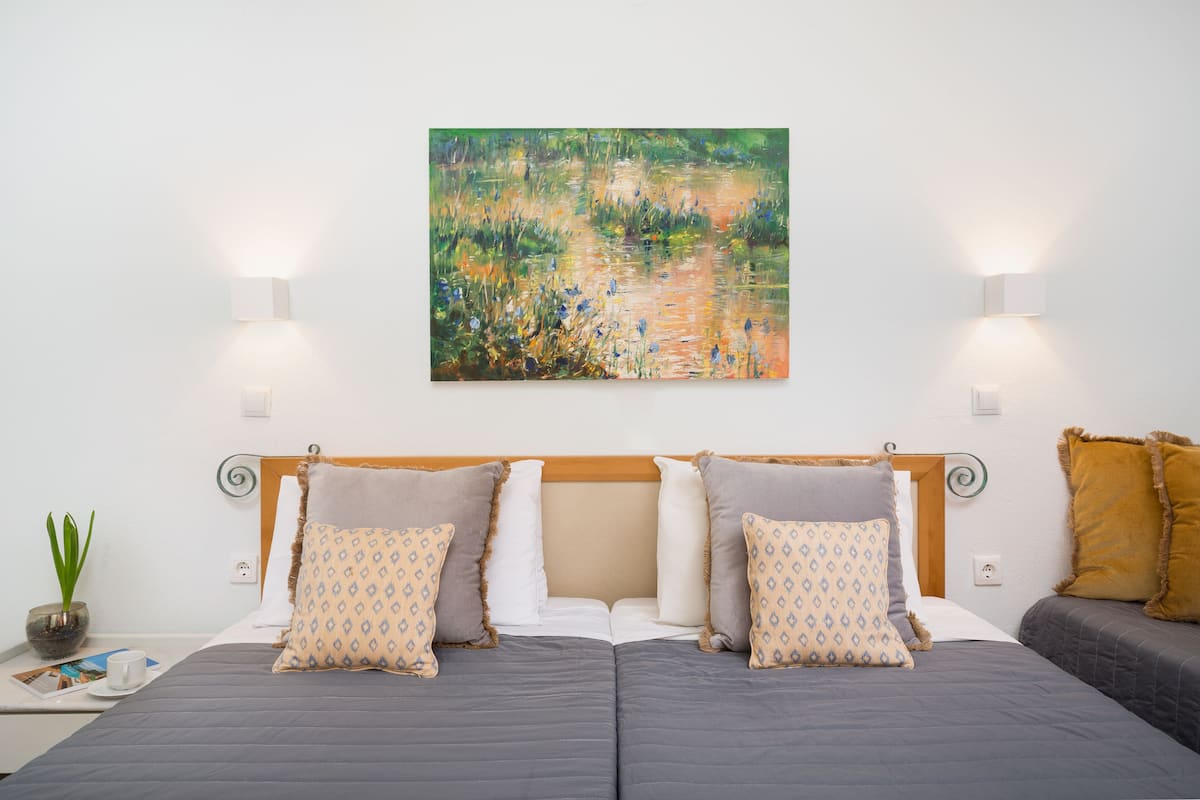 A double bed with a headboard, two bedside tables, a potted plant, and a painting on the wall.