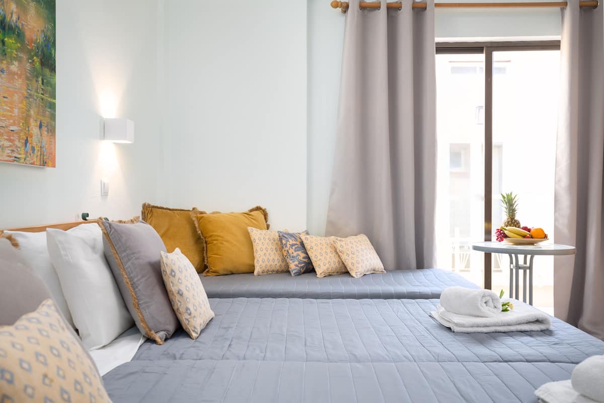 A hotel room with a bed, pillows, a small table with fruit, and a view of the outside.