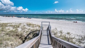 A wooden boardwalk leading to a beach with clear skies and calm waters.
