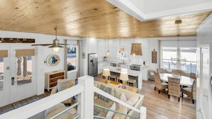 A spacious living area with a high ceiling, wooden beams, and a central seating area with a dining table.