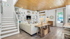 A modern living room with a white sofa, wooden flooring, a staircase, and a ceiling fan.