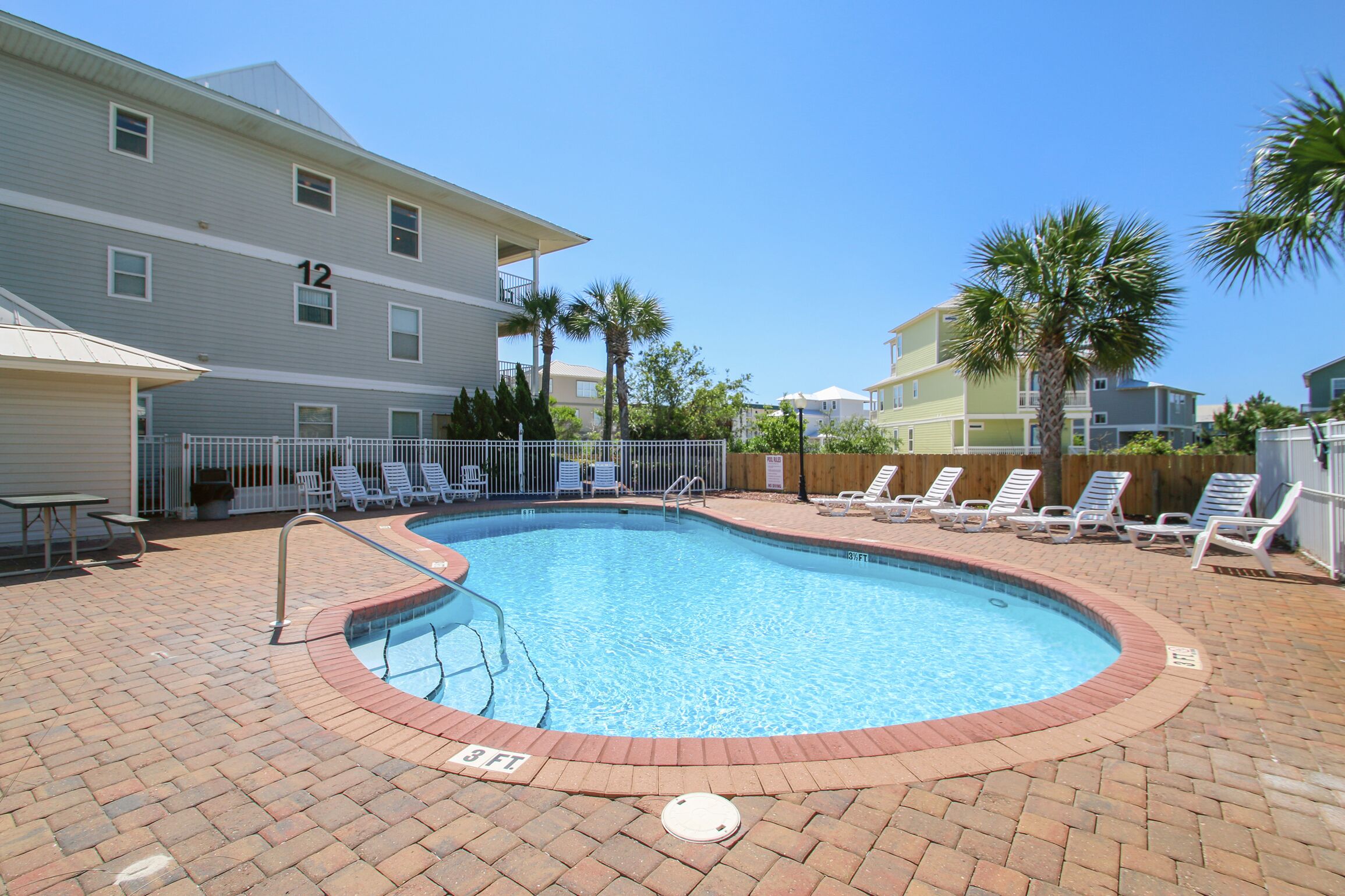 A swimming pool with a brick border, surrounded by lounge chairs and a fence.