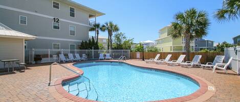 A swimming pool with a brick border, surrounded by lounge chairs and a fence.