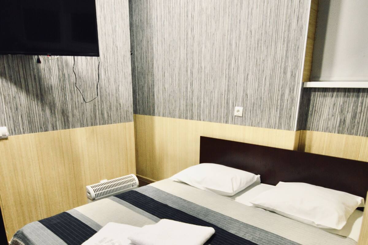 Una habitación de hotel con una cama, un televisor de pantalla plana en la pared y suelo de madera.