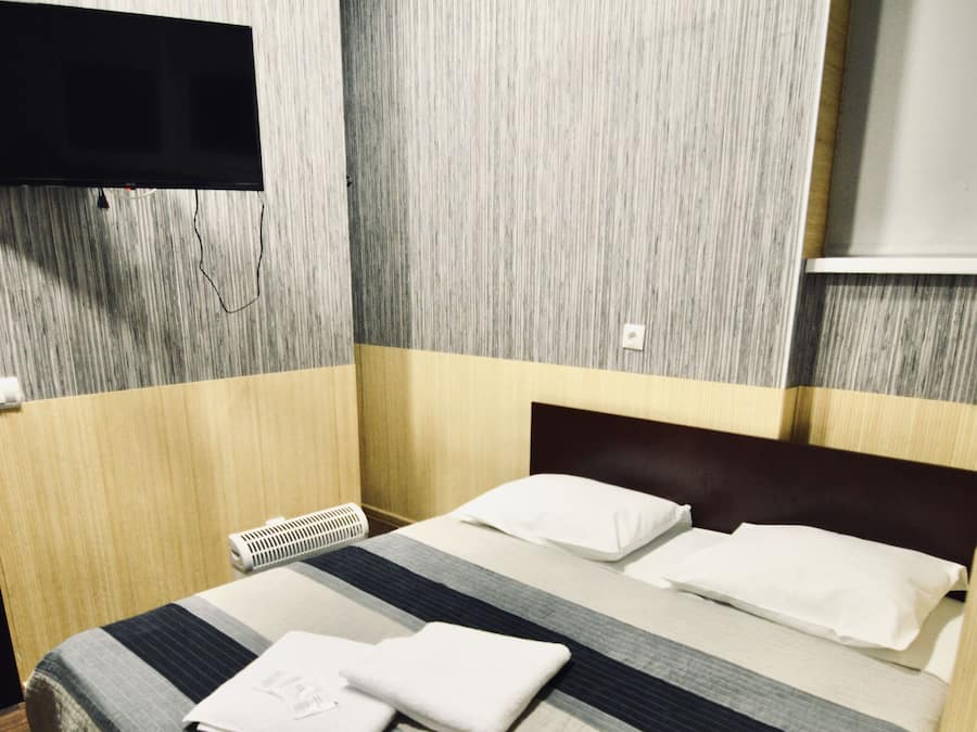 A hotel room with a bed, a flat-screen TV mounted on the wall, and a wooden floor.
