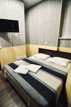A hotel room with a bed, a flat-screen TV mounted on the wall, and a wooden floor. - UNO Apart Hotel (Kyiv)