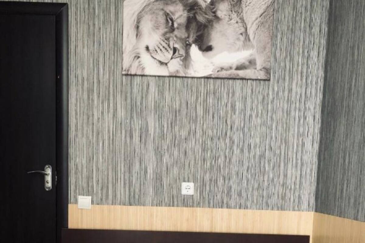 Una habitación de hotel con cama, cabecera de madera, pared texturizada de color gris y un cuadro con leones.