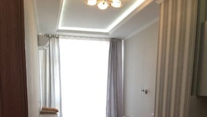 Une pièce de taille modeste, comprenant un canapé, une petite table et une chaise. On y trouve une fenêtre avec des rideaux, une porte et un luminaire au plafond.