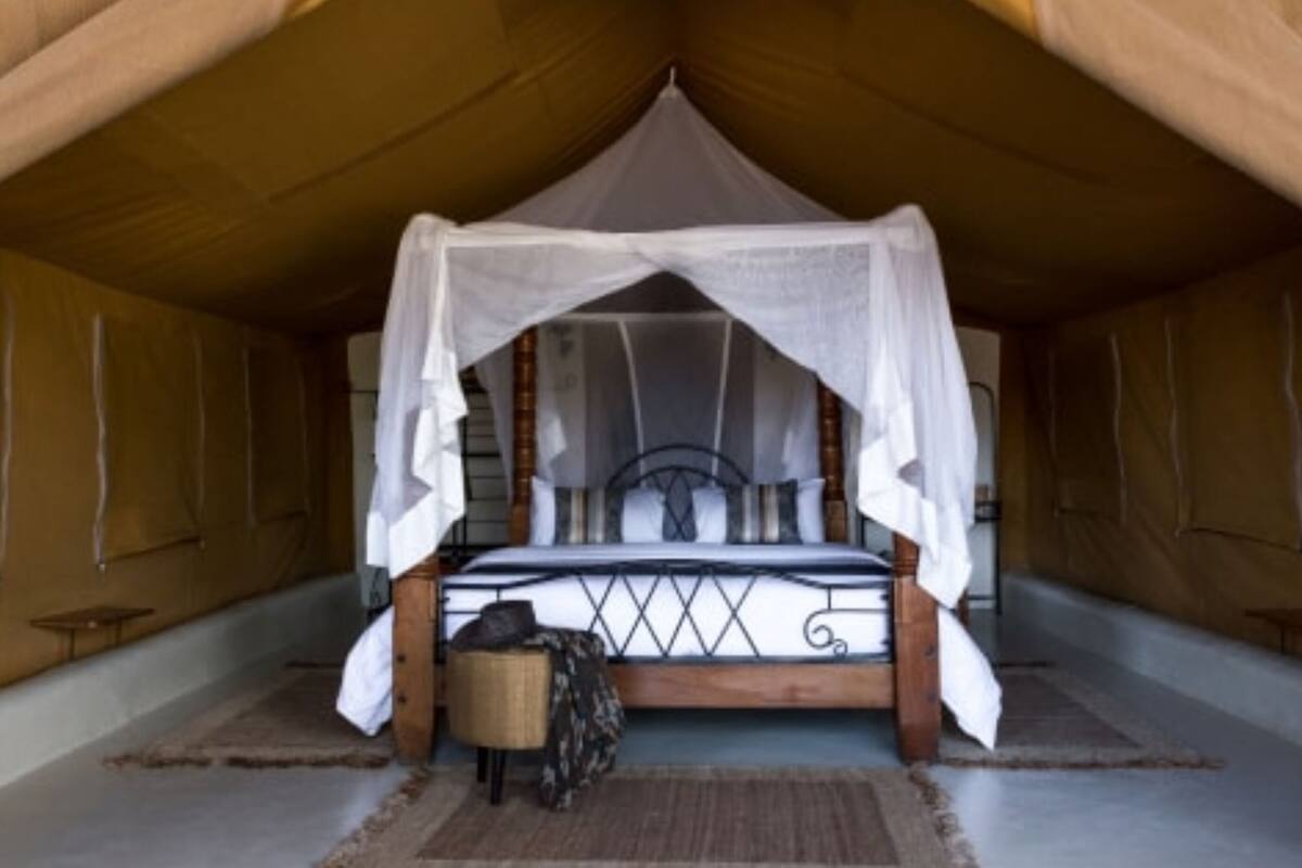Quarto com tenda, cama sob um dossel, uma pequena mesa e uma cadeira.