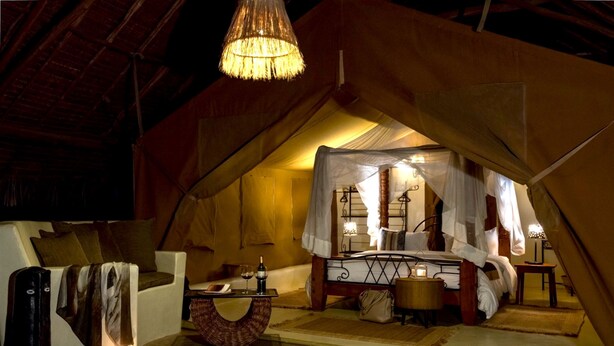 A cozy tented accommodation with a bed, bedside table, lamp, and a hanging light fixture. - Flamingo Hill Tented Camp (Nakuru)