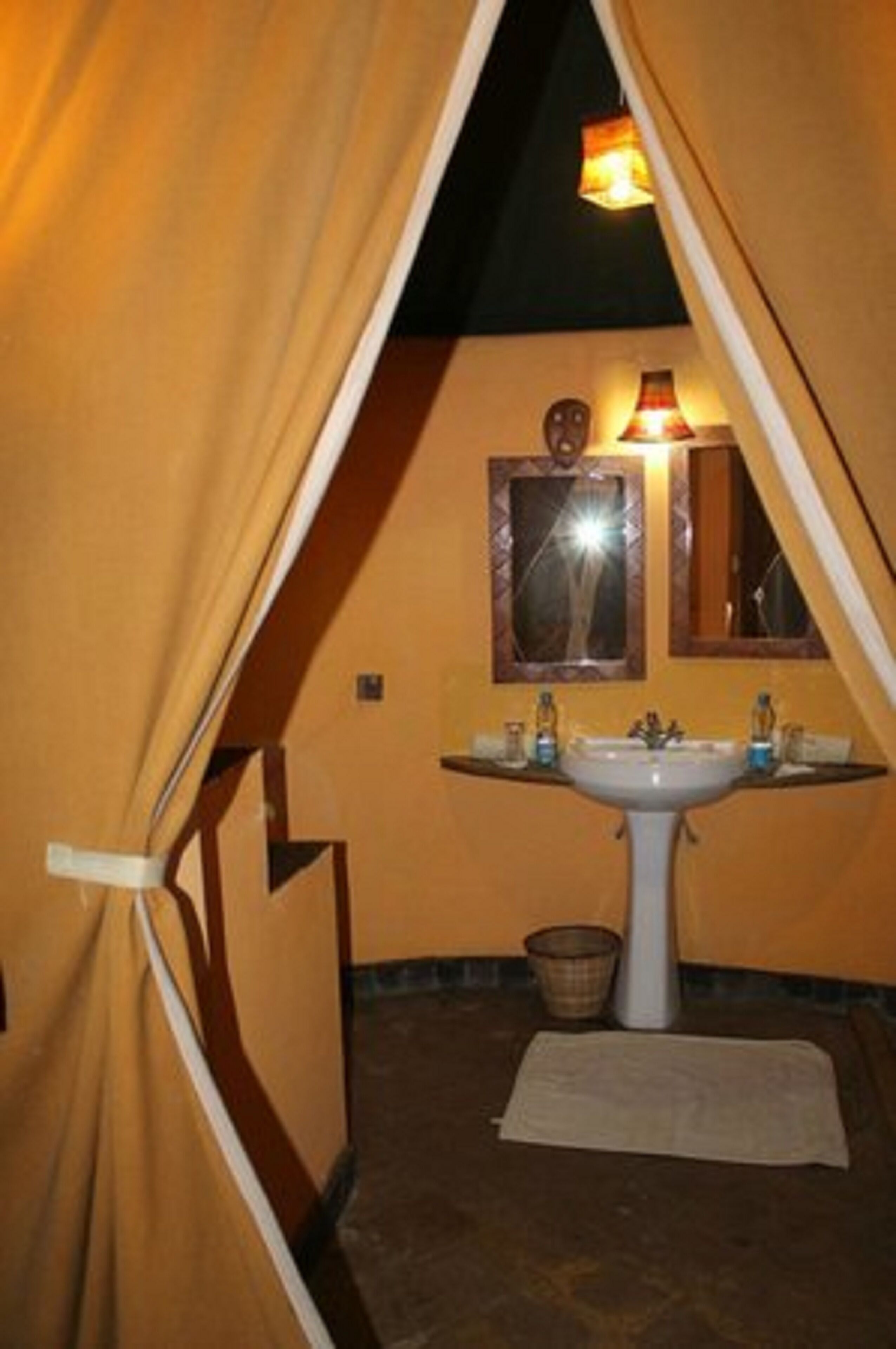 Une petite salle de bain triangulaire, avec un lavabo, des miroirs et une serviette sur le sol.