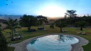 A swimming pool with a stone border, surrounded by grass and trees, with a view of the horizon. - Flamingo Hill Tented Camp (Nakuru)