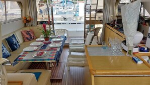 Een eethoek met een tafel gedekt voor twee personen, een bank met marinekussens, en een uitzicht op boten door de ramen.