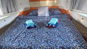 Een klein bed met een bloemenbedekking, een hoofdbord en een raam met gordijnen.