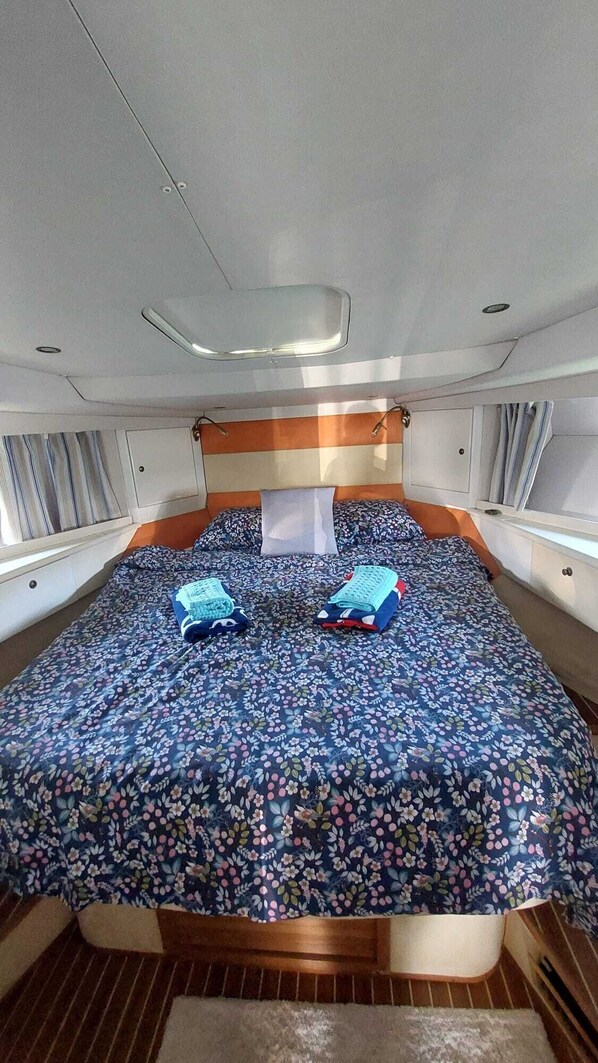 A compact bed with a floral bedspread, a headboard, and a window with curtains.