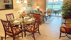 A dining area with a glass table surrounded by wooden chairs, a chandelier, and a view of a golf course through large sliding doors.