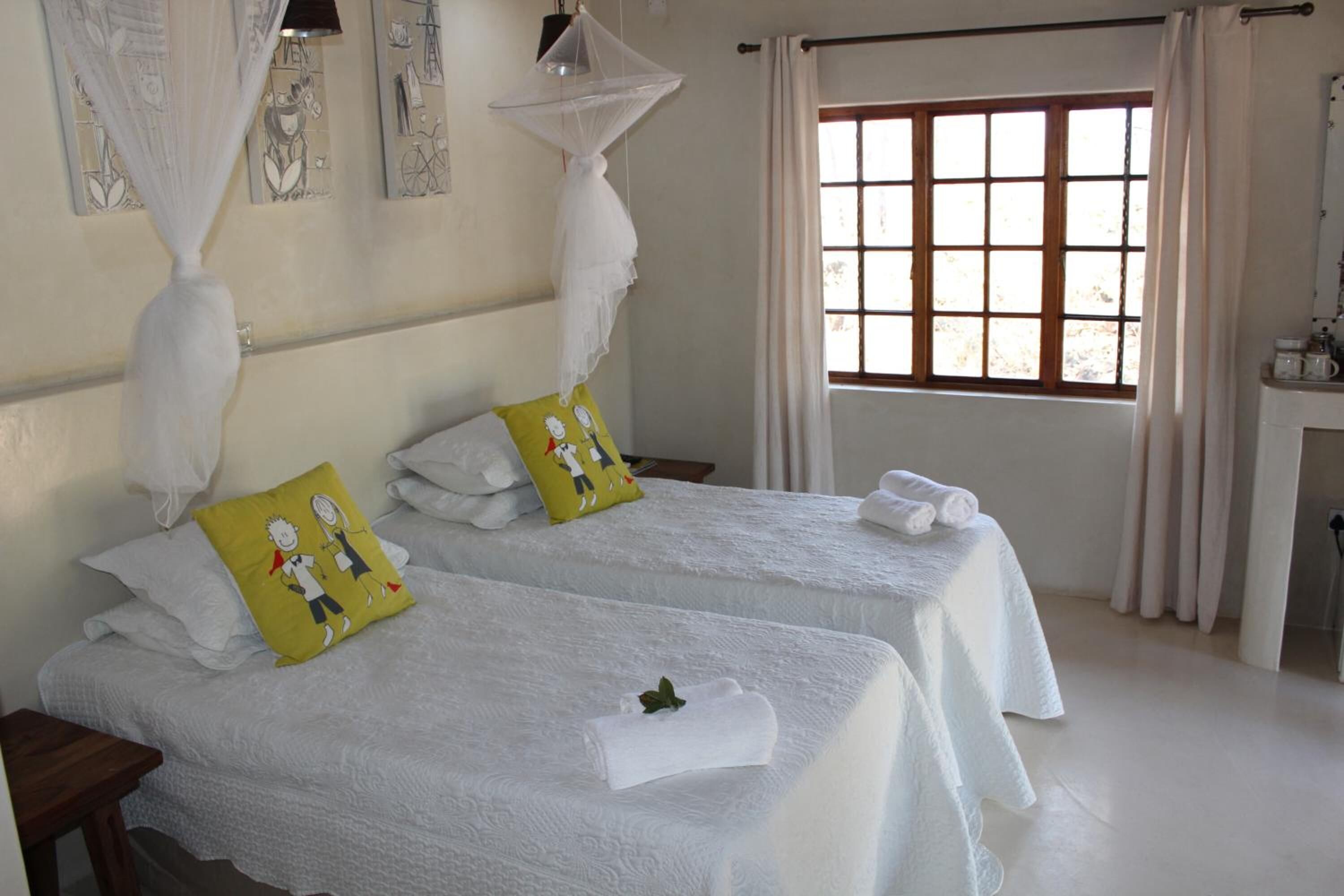 A hotel room with two beds, white bedding, a window with curtains, and artwork on the walls.