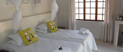 A hotel room with two beds, white bedding, a window with curtains, and artwork on the walls.