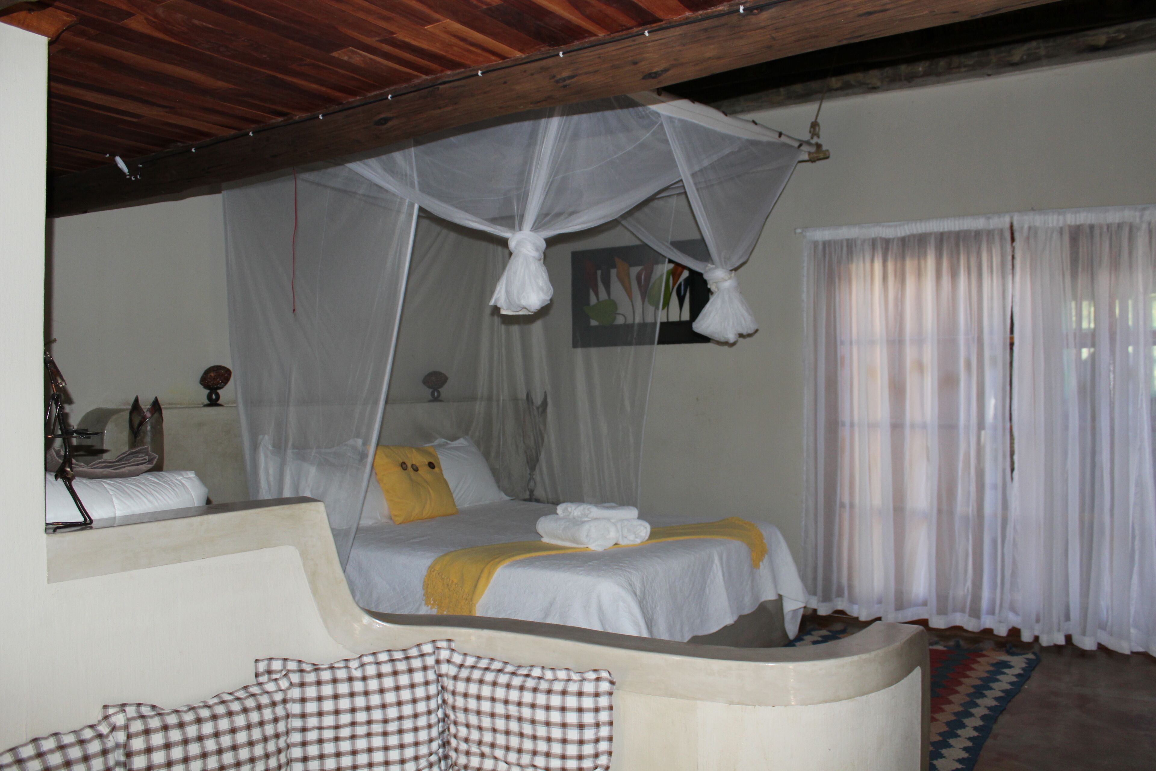 A bedroom with a bed, a canopy, a bedside table, and a window with curtains.