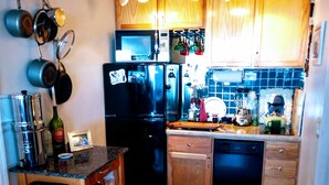 Una cocina compacta con armarios de madera, un refrigerador negro y una alfombra de cuero de vaca.