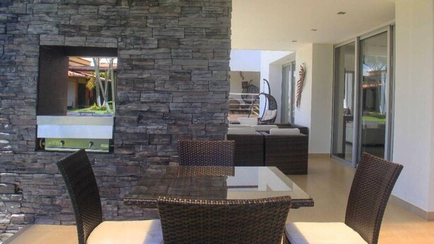 A modern dining area with a stone wall, a glass table, and wicker chairs. - CERRITOS ... NATURE, BEAUTY AND FUN !! (Pereira)