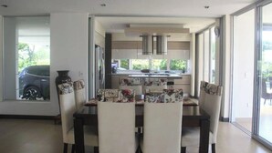 A modern dining area with a large table and chairs, a kitchen in the background, and a view of a parked car through a window. - CERRITOS ... NATURE, BEAUTY AND FUN !! (Pereira)
