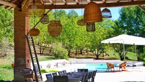 An outdoor dining area with wicker hanging lights, a pool, and a white umbrella. - L'Ostalas (Lafrancaise)