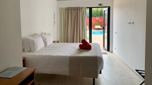 Ein Hotelzimmer mit Bett, einer Bank, einem Fenster mit Vorhängen und Blick auf einen Pool und Sitzgelegenheiten im Freien.