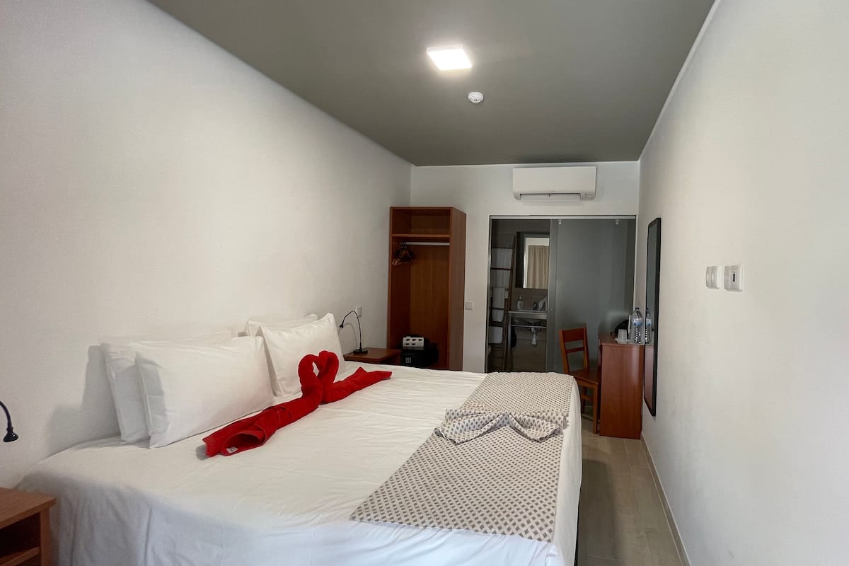 A hotel room with a bed, a wardrobe, a desk with a chair, and a bathroom visible through an open door.