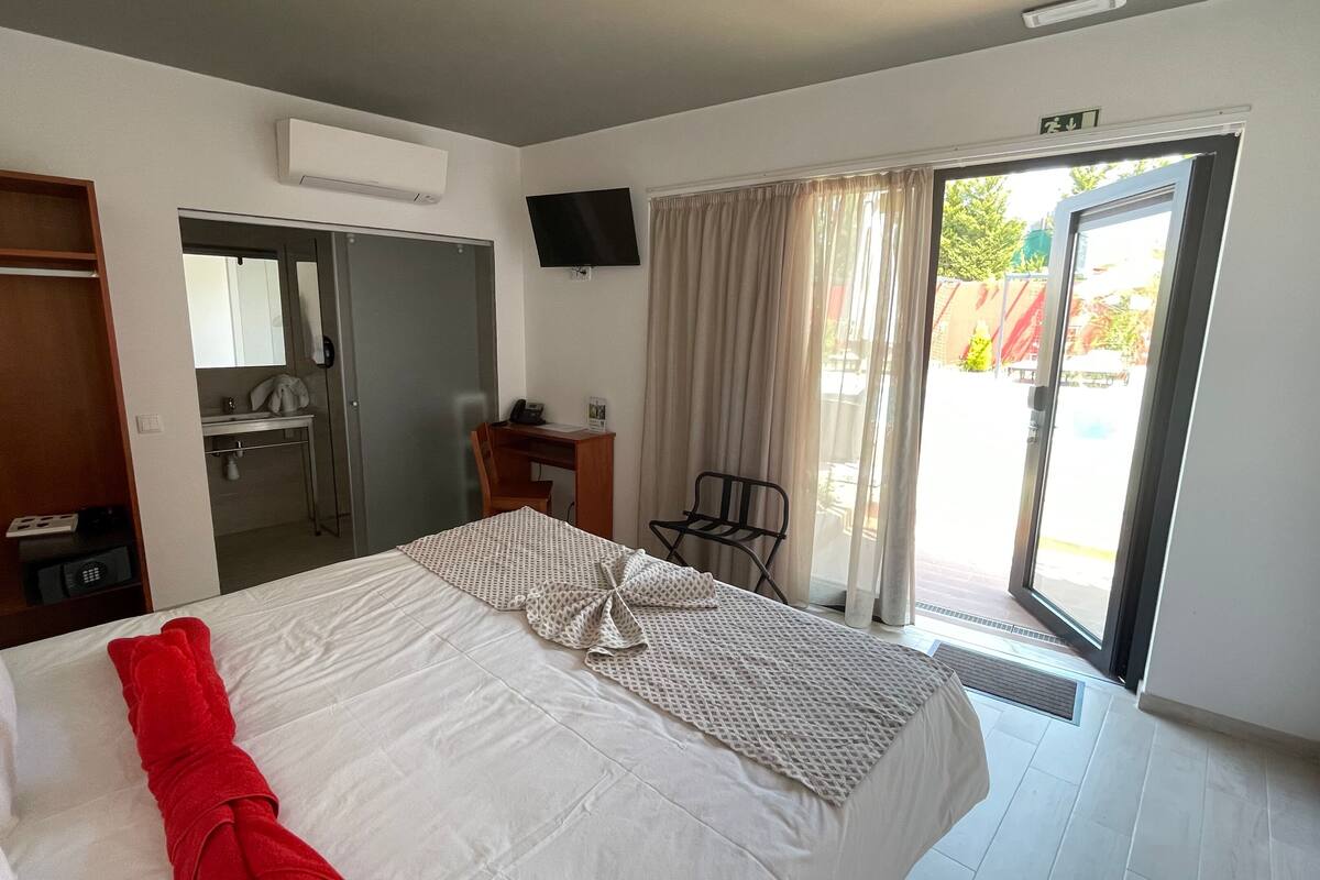 A hotel room with a bed, a desk, a chair, a TV, and a sliding glass door to the outside.