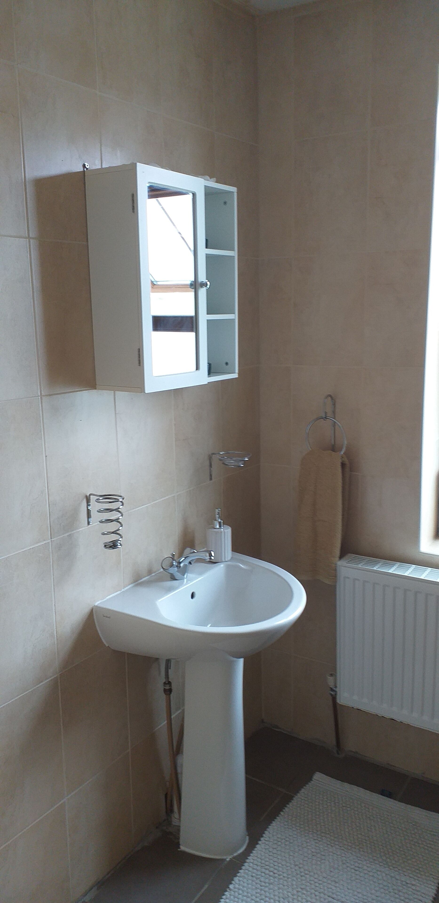A bathroom with a white sink, a cabinet, and a towel hanging on a hook.