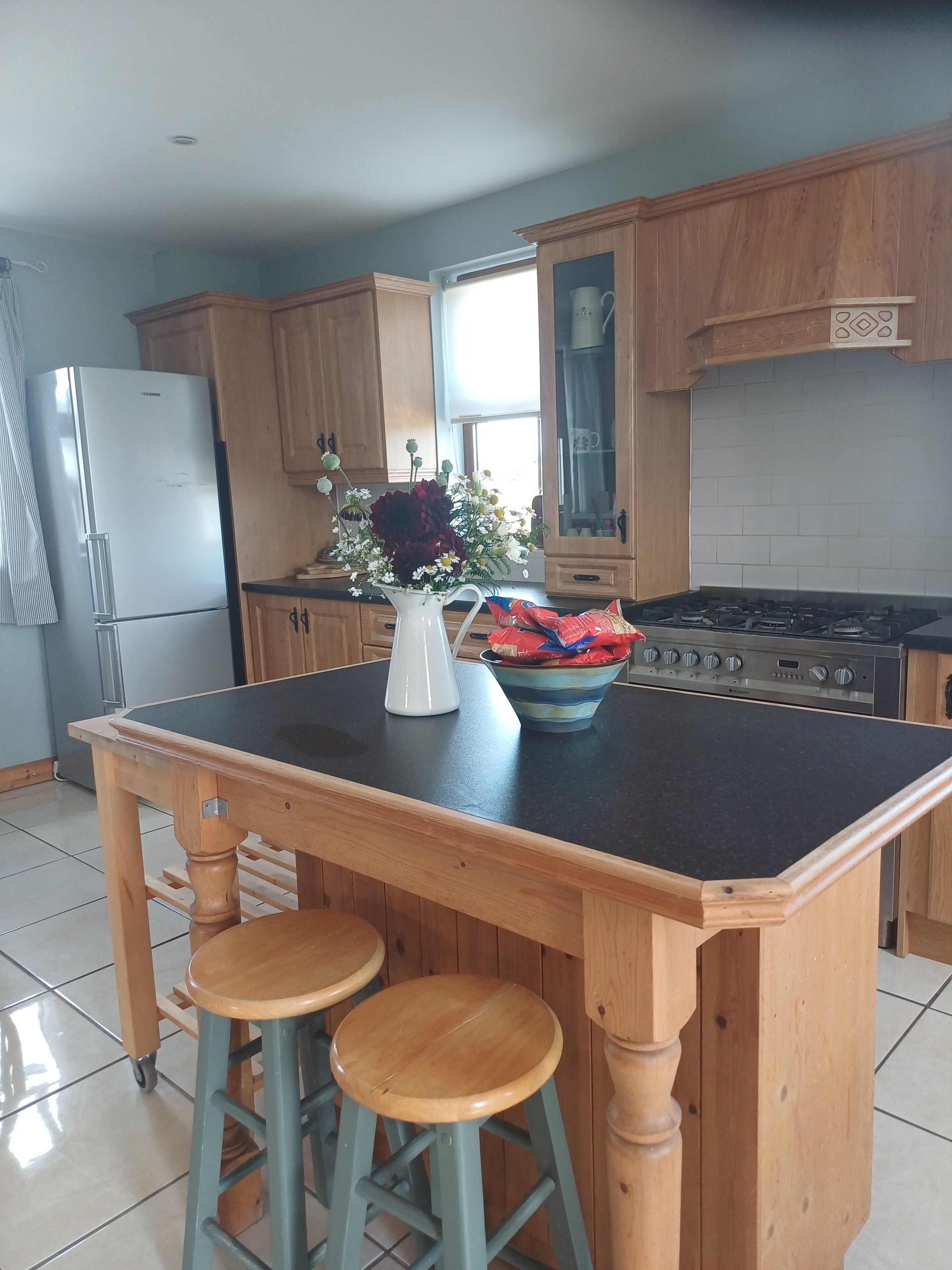 A kitchen with wooden cabinets, a black countertop island with stools, a refrigerator, and a stove.