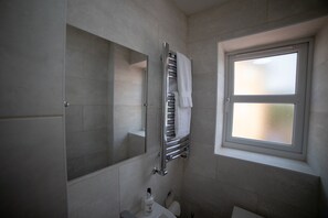 A bathroom with a large mirror, a towel rack, a window, and a toilet. - The Coach House by Riis Property (Staines)