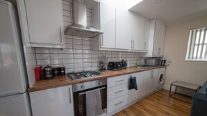 A modern kitchen with white cabinets, a wooden countertop, a gas stove, a microwave, and a built-in oven. - The Coach House by Riis Property (Staines)