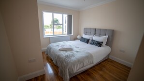A bedroom with a large bed, a window, and wooden flooring. - The Coach House by Riis Property (Staines)
