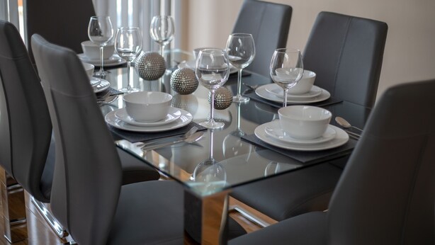 A dining table set with white plates, bowls, and wine glasses, surrounded by black chairs. - The Coach House by Riis Property (Staines)