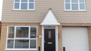 A two-story building with a black front door, a garage door, and a window with a metal gate. - The Coach House by Riis Property (Staines)