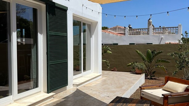 A modern patio with a wooden table and chairs, a large sliding glass door, and a string of lights. - Villa with private pool in Cap d'Artrutx. (Cala en Bosc)