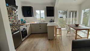 A modern kitchen with a central island, a dining area with a table and chairs, and large windows offering a view of the outdoors. - Villa with private pool in Cap d'Artrutx. (Cala en Bosc)