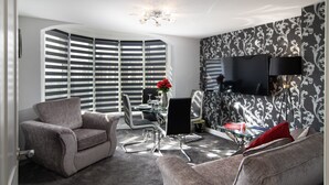 A modern living room with a curved wall, a flat-screen TV mounted on the wall, a glass coffee table, and two grey sofas. - 2 Bedrooms Sleeps 6 Near Top Blackpool Attractions (Blackpool)