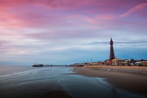 A coastal town with a prominent tower, a pier extending into the sea, and a beach area.