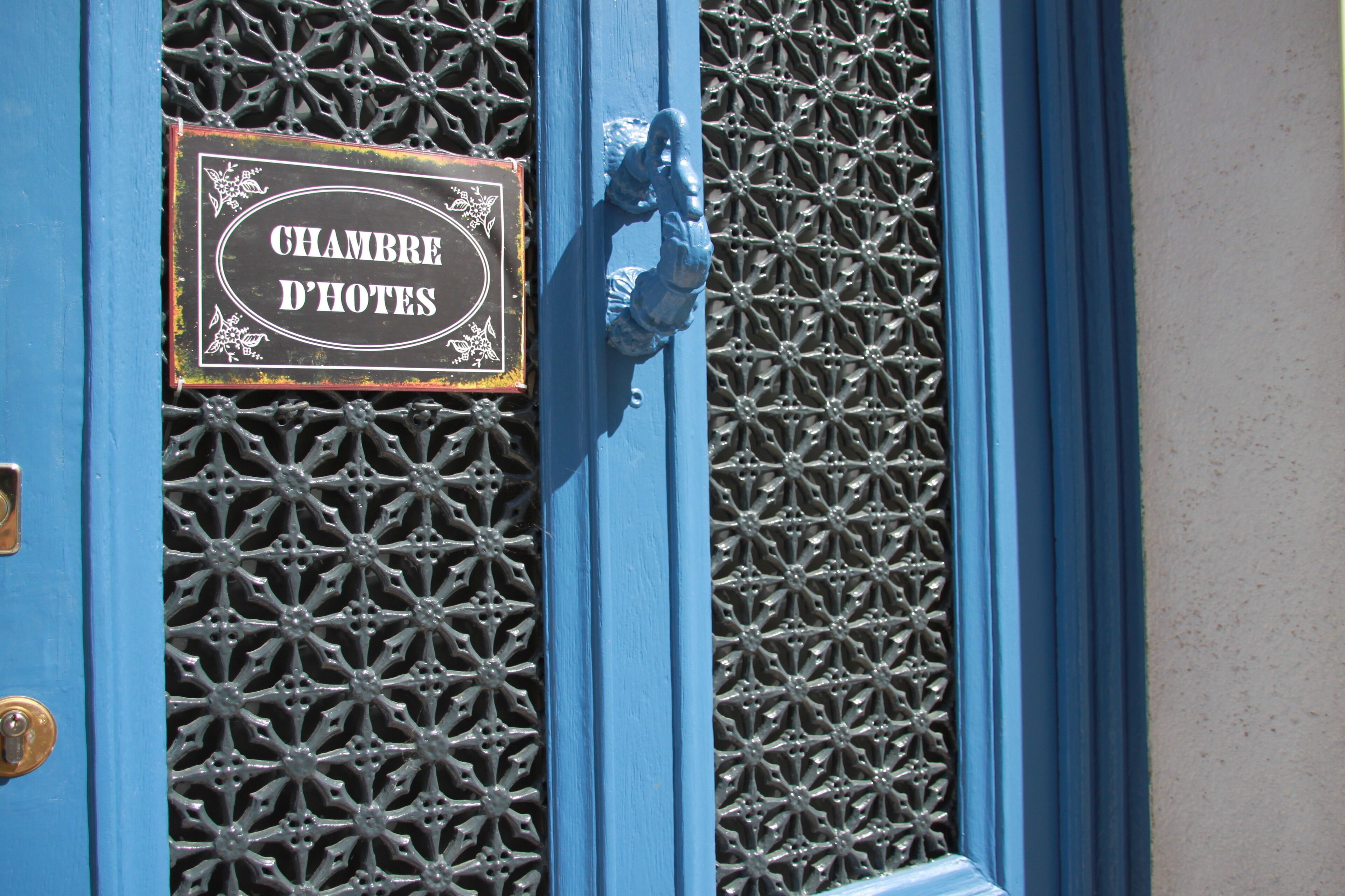 A blue door with a sign reading "CHAMBRE D'HOTES" and a decorative metal grille.