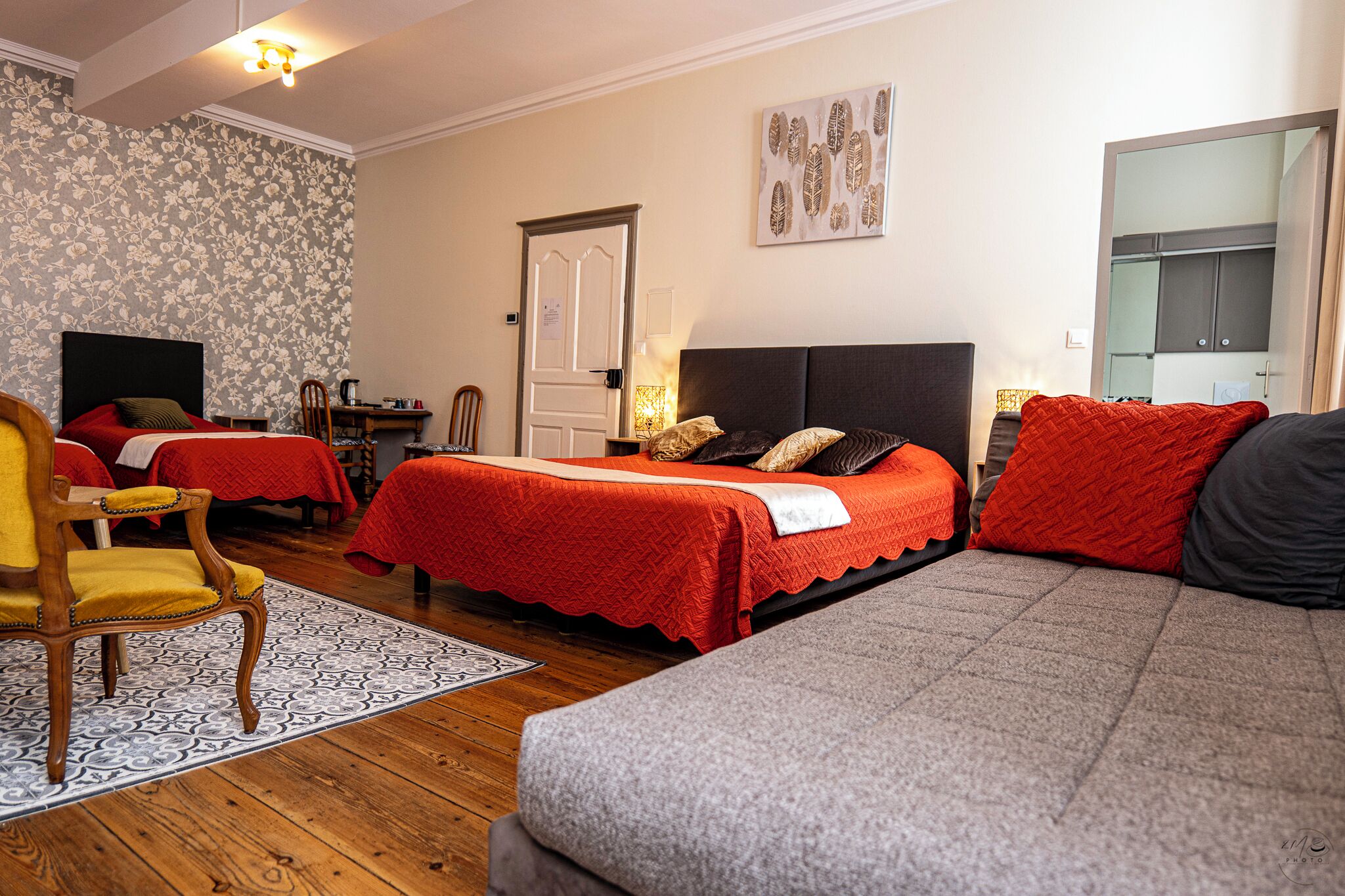 A hotel room with two beds, a sofa, a wooden chair, a desk, and a mirror.