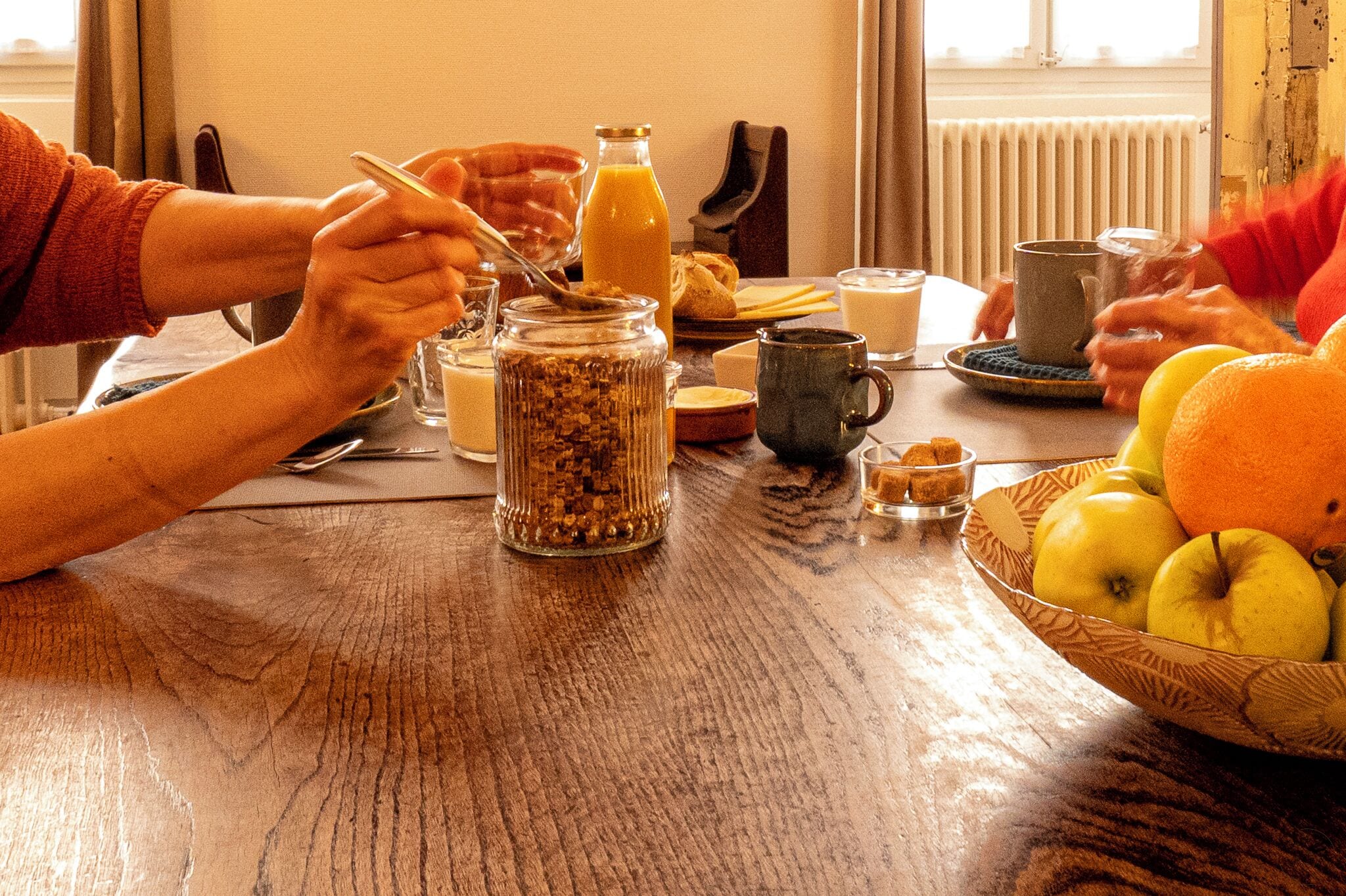 Ett matbord i trä med frukosttillbehör, inklusive en glasburk med flingor, en flaska apelsinjuice och en skål med frukt.