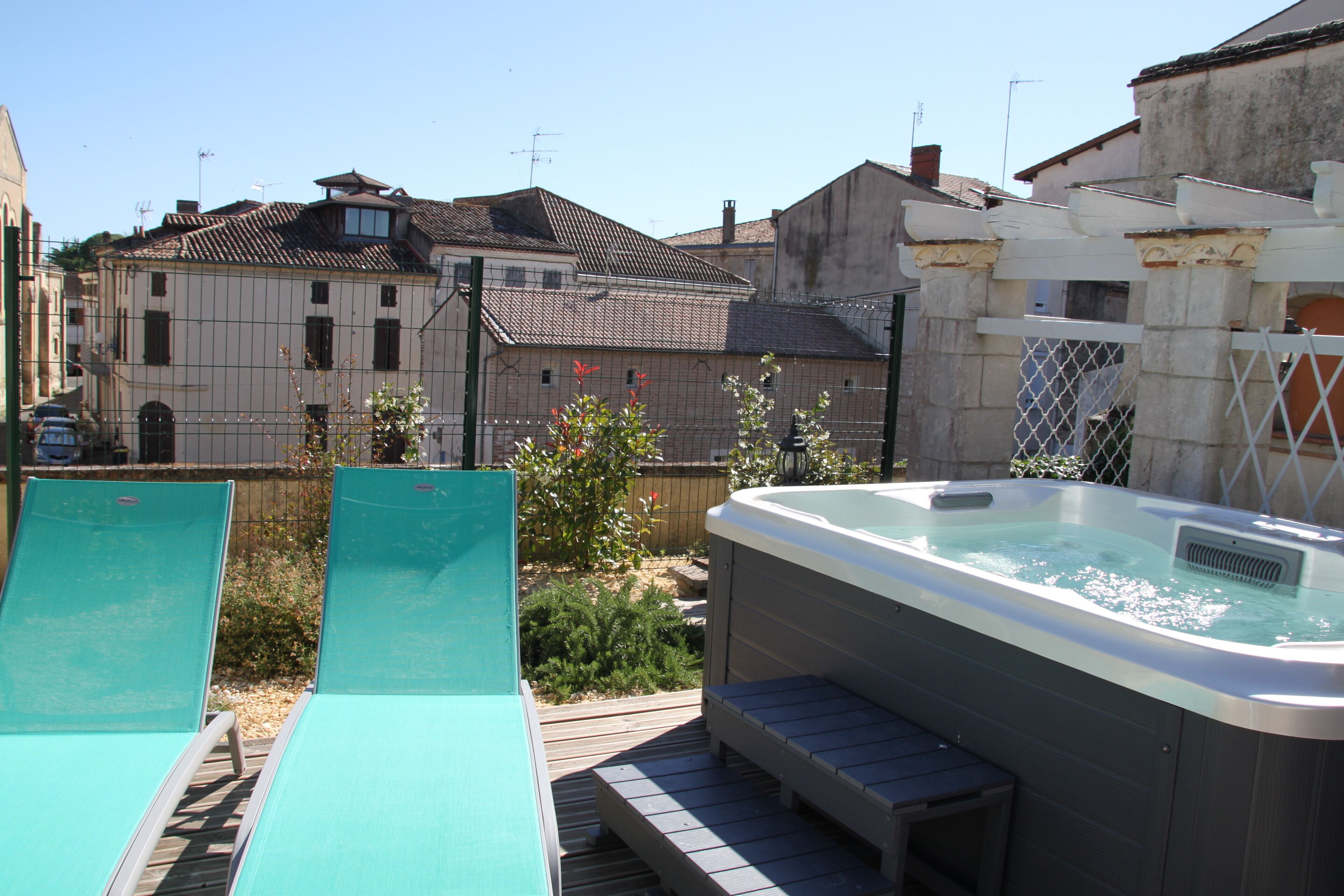 A backyard with a hot tub, two lounge chairs, and a wooden deck.