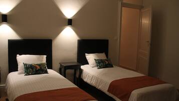 A hotel room with two beds, each with a headboard, a small table, and wall-mounted lighting.